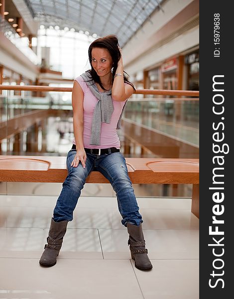 Portrait of a cute brunette on a bench over mall background. Portrait of a cute brunette on a bench over mall background