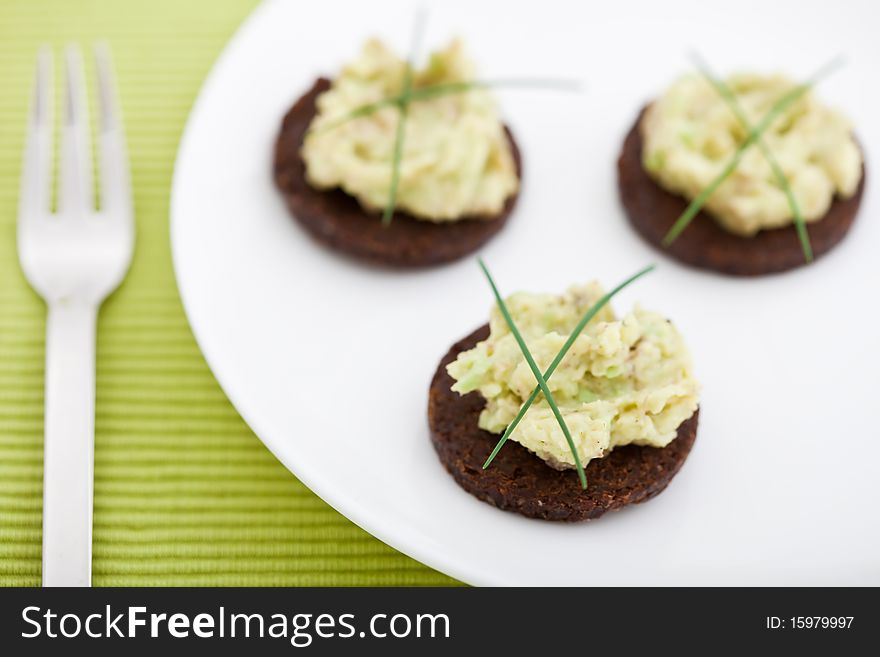 Three pumpernickel slices with guacamole on a white plate. Shallow DOF