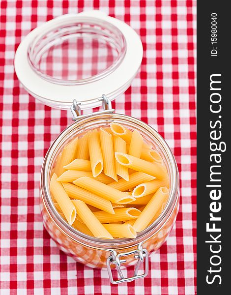 Uncooked pasta in a glass jar on a red and white background. Shallow DOF