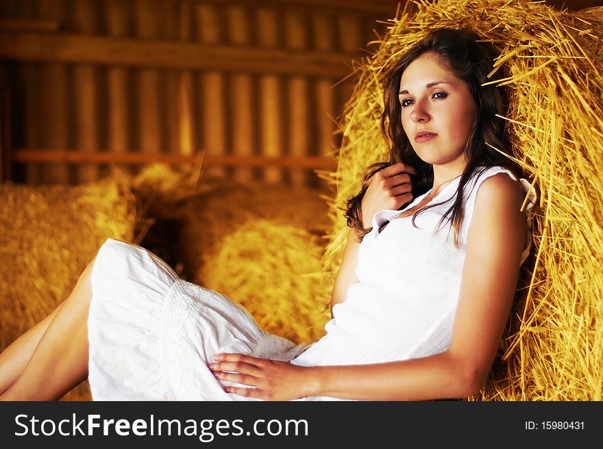 A young and cute woman in a white dress is resting on the hay. Image taken in an old shed. A young and cute woman in a white dress is resting on the hay. Image taken in an old shed.