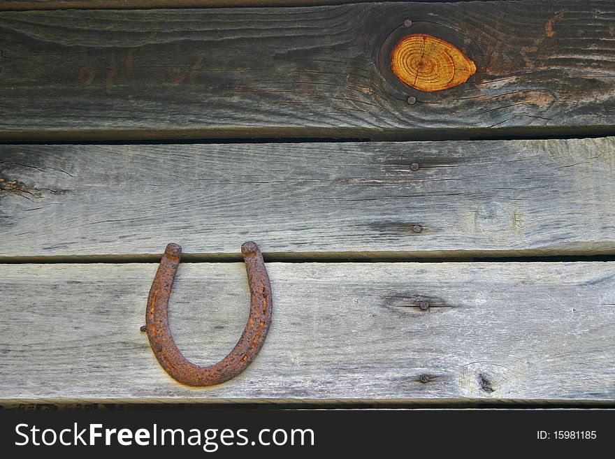 A rusty horseshoe hangs on a barn wall, with a prominent knot in one of the planks. A rusty horseshoe hangs on a barn wall, with a prominent knot in one of the planks