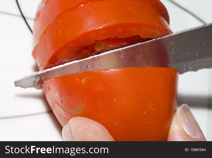 A Tomato being cutted on board. A Tomato being cutted on board