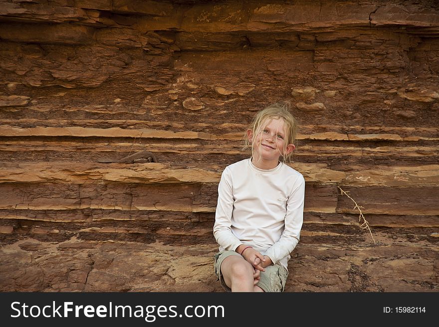 Young girl sitting before orange rocks in the desert. Young girl sitting before orange rocks in the desert