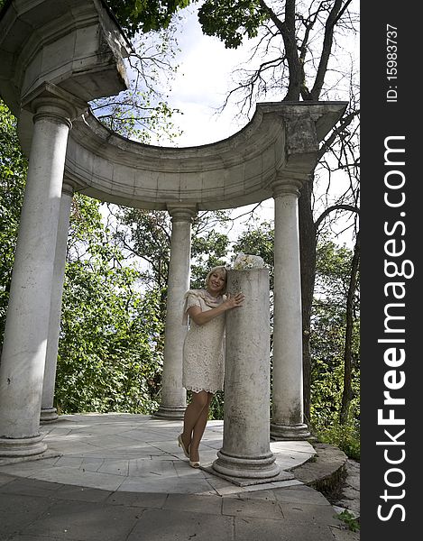 The elegant woman costs at the broken column with a bunch of flowers in an arbor a rotunda. The elegant woman costs at the broken column with a bunch of flowers in an arbor a rotunda