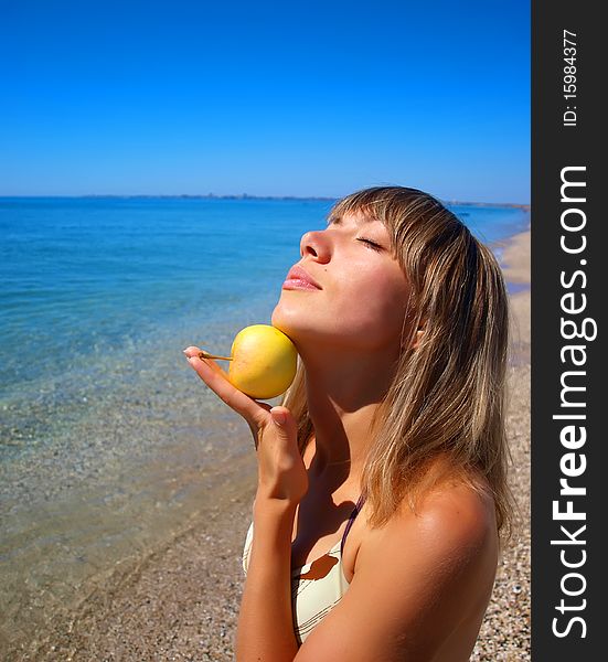 Beautiful young woman with apple on seashore