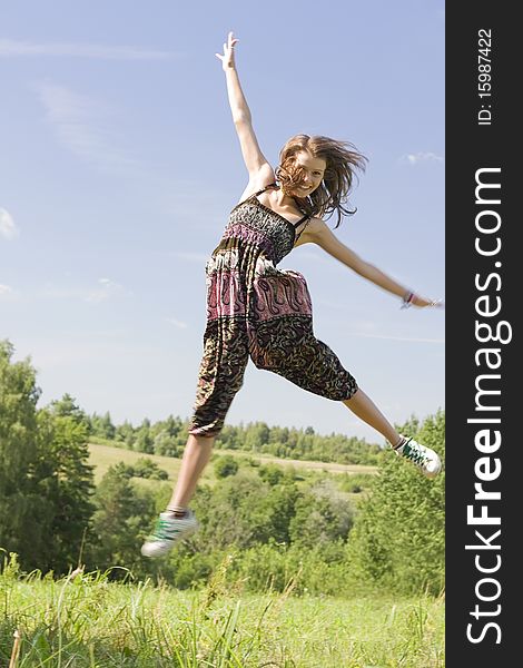 Young happy woman jumping on a green meadow with a cloudy sky