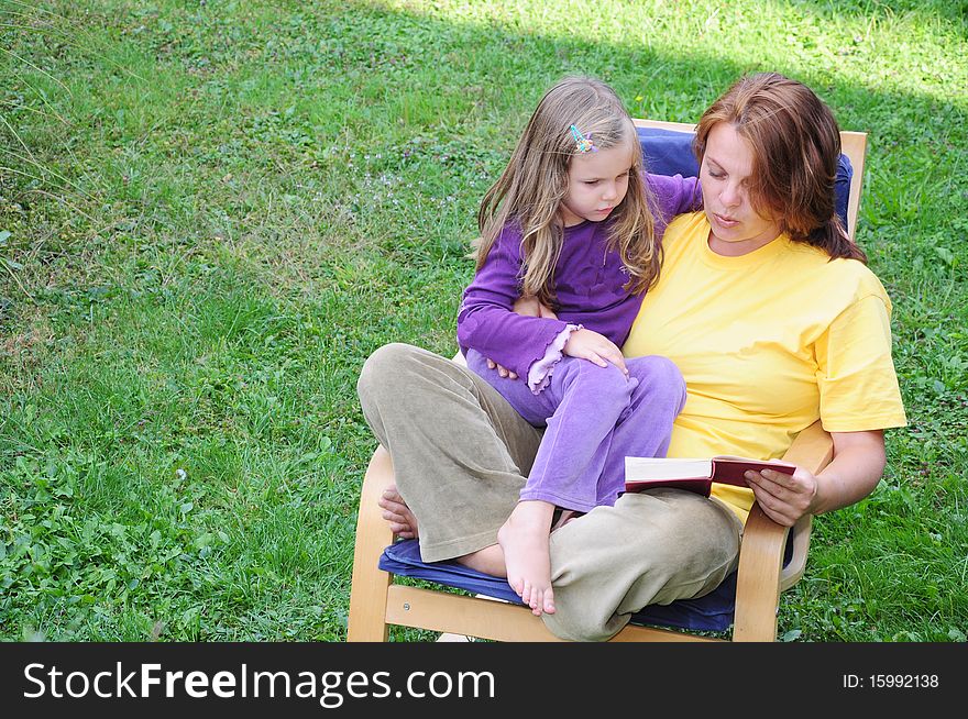 Mother and daughter have fun reading the book in the yard. Mother and daughter have fun reading the book in the yard