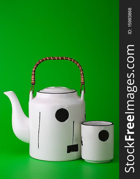 White porcelain teapot with wooden handle and cup on  bright green background. White porcelain teapot with wooden handle and cup on  bright green background