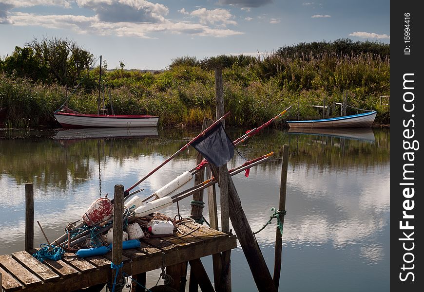 Flags and other fishing gear resting on small primitive wooden pier with boats and meadow in the background. Flags and other fishing gear resting on small primitive wooden pier with boats and meadow in the background.