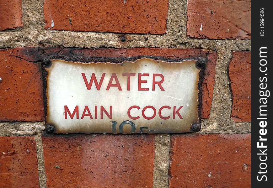 Red brick wall with aged water mains sign that has rusted. Red brick wall with aged water mains sign that has rusted