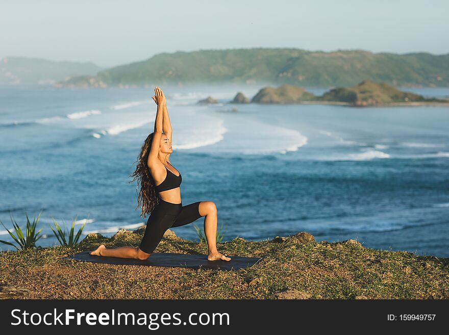 Woman practicing yoga outdoors with amazing ocean and mountain view