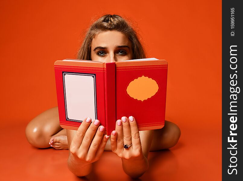 Beautiful young fitness woman doing yoga, stretching her leg, reading a book on studio backdrop orange background. athletic girl e