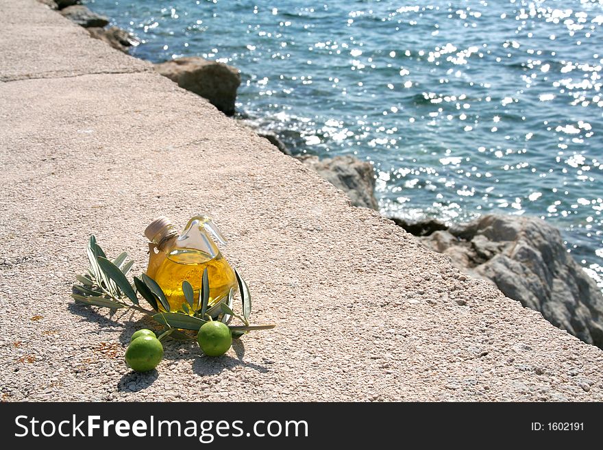 Small bottle of olive-oil an an olive-branch with fruits on it in front of a mediterranean scene. Small bottle of olive-oil an an olive-branch with fruits on it in front of a mediterranean scene