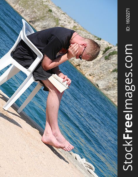 Man on vacation in front of the sea, relaxing while reading. Man on vacation in front of the sea, relaxing while reading