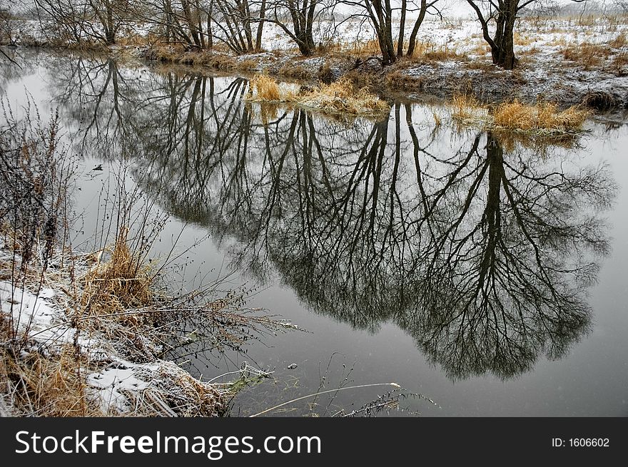 The country river in the beginning of winter with reflection of a local landscape