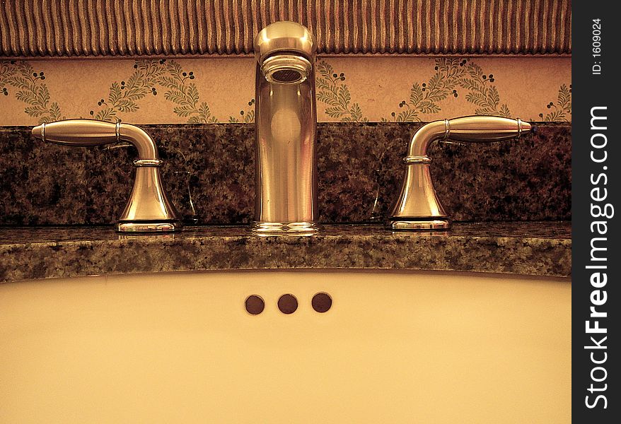 A bathroom faucet and sink closeup with green patterned wallpaper