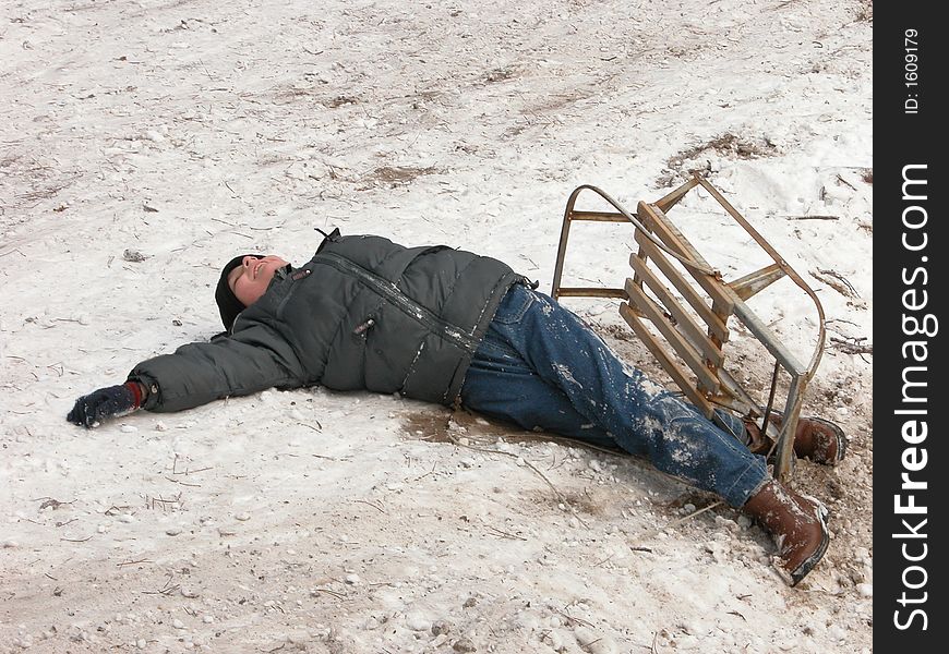 The boy sprawling on the snow near the upturned sledge. The boy sprawling on the snow near the upturned sledge