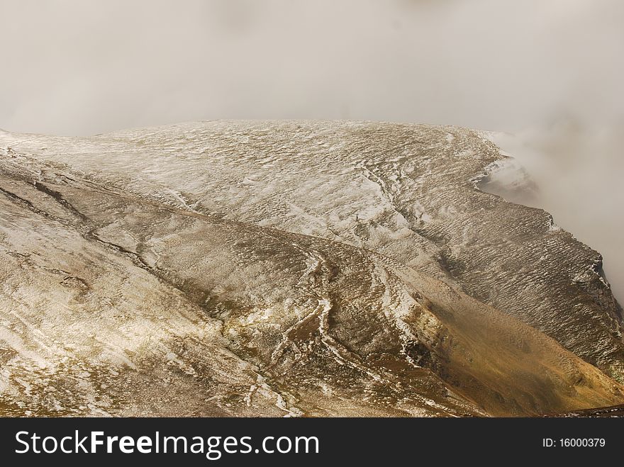 Cloudy mountain covered with dry grass and snow, fog on one side and sun spots