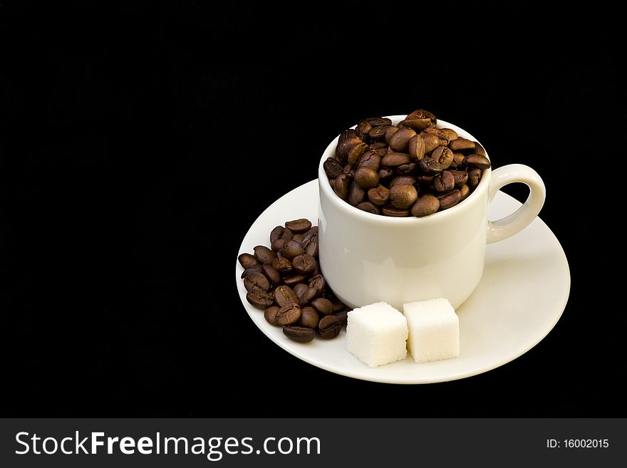 White cup with coffee beans and sugar on black