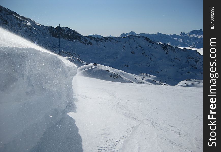 A breeze blowing ice crystals from the top of a snowdrift across a ski run in the French Alps. A breeze blowing ice crystals from the top of a snowdrift across a ski run in the French Alps.