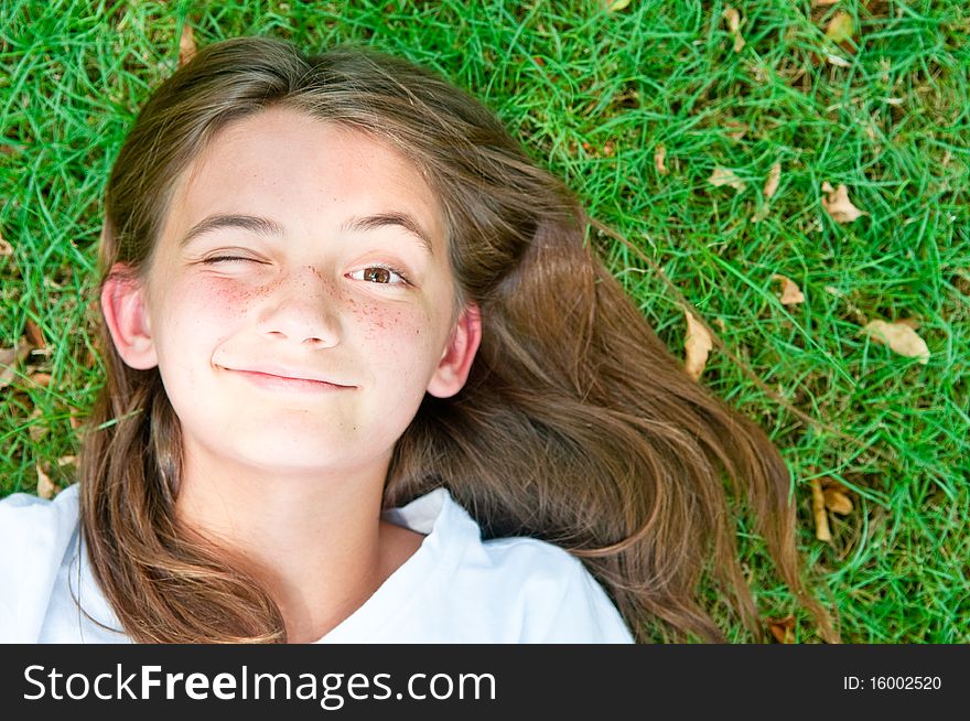 A happy young girl resting on the grass winks at the camera. A happy young girl resting on the grass winks at the camera