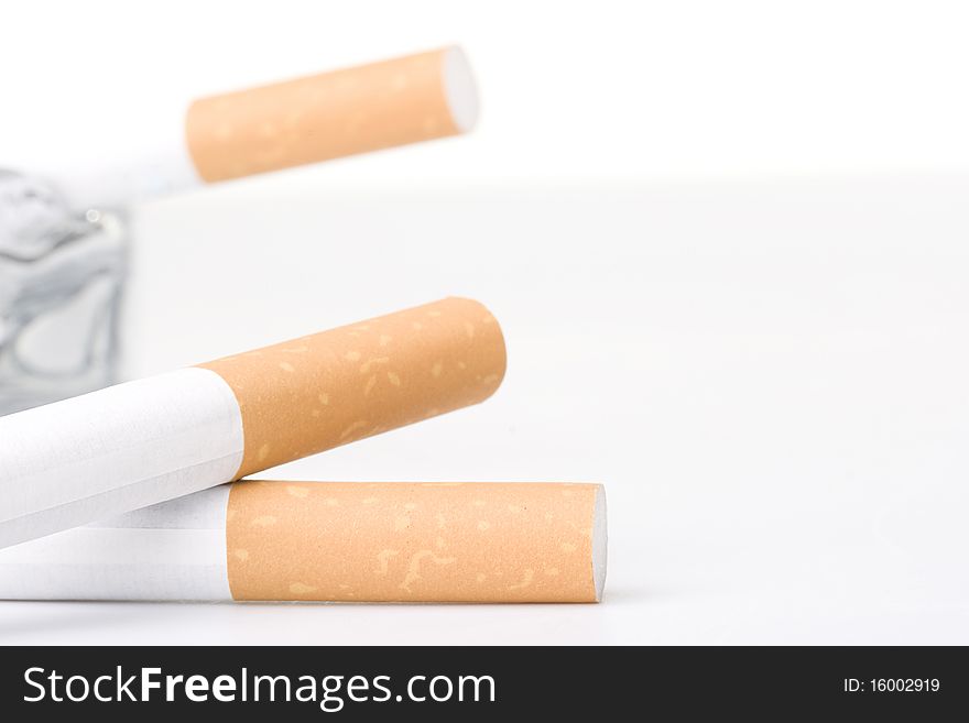 Two filtered cigarettes laying in front of a glass ashtray.