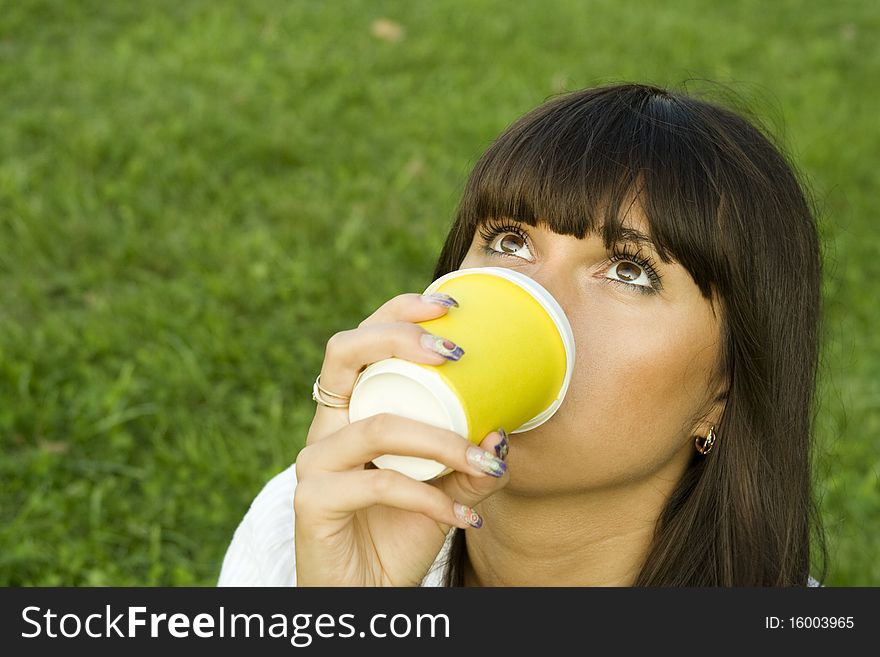 A beautiful young woman relaxing in the park. Drinking coffee from paper cups. Portrait. A beautiful young woman relaxing in the park. Drinking coffee from paper cups. Portrait