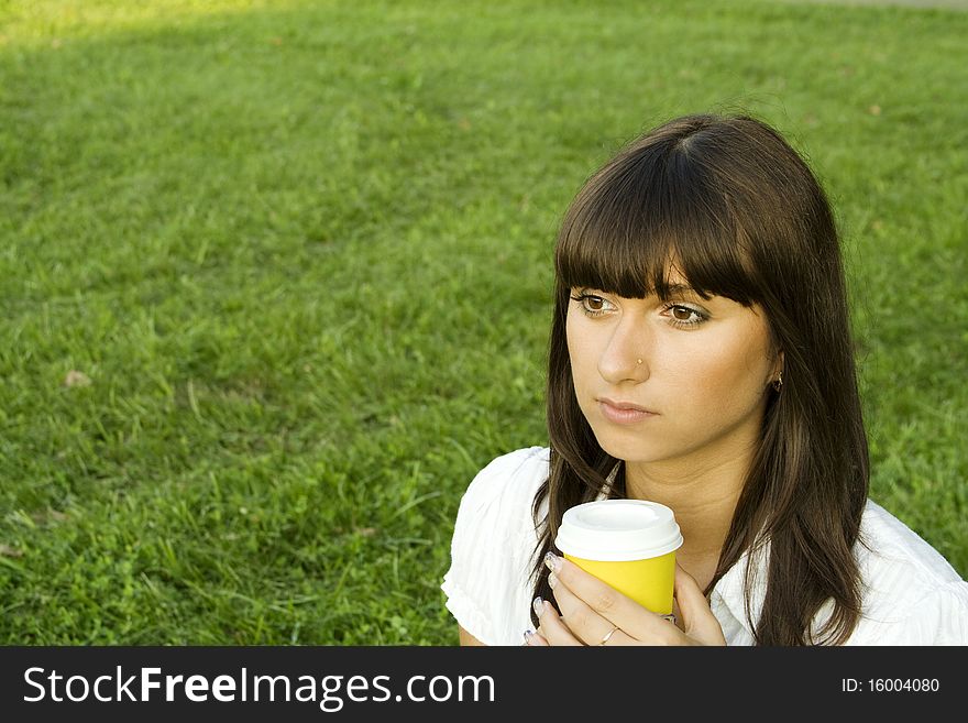 Beautiful young woman relaxing in the park. Holding a paper cup of coffee. Portrait. Beautiful young woman relaxing in the park. Holding a paper cup of coffee. Portrait