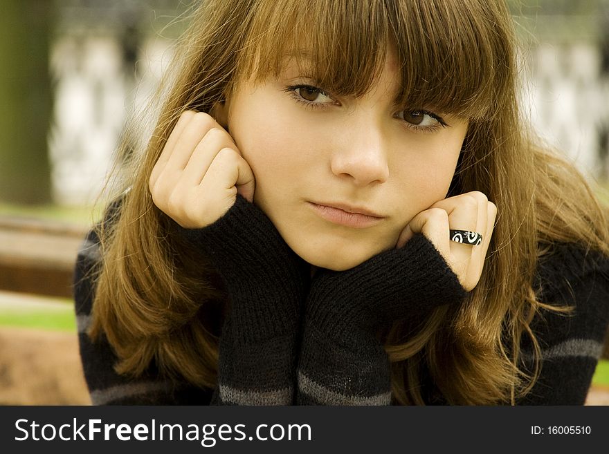 Beautiful young girl in a sweater in the autumn grieves in the park sitting on the bench. Beautiful young girl in a sweater in the autumn grieves in the park sitting on the bench