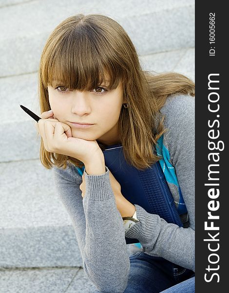 Schoolgirl sitting on the stairs with a notebook and pen. Thinking
