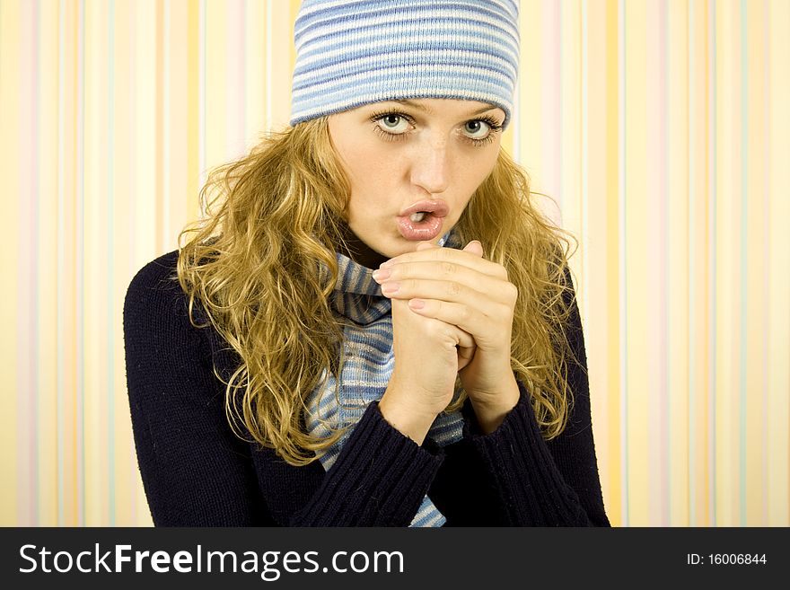 Photo of a young woman in a blue sweater with a blue knit cap and scarf. She breathes on his hands to warm them. Photo of a young woman in a blue sweater with a blue knit cap and scarf. She breathes on his hands to warm them