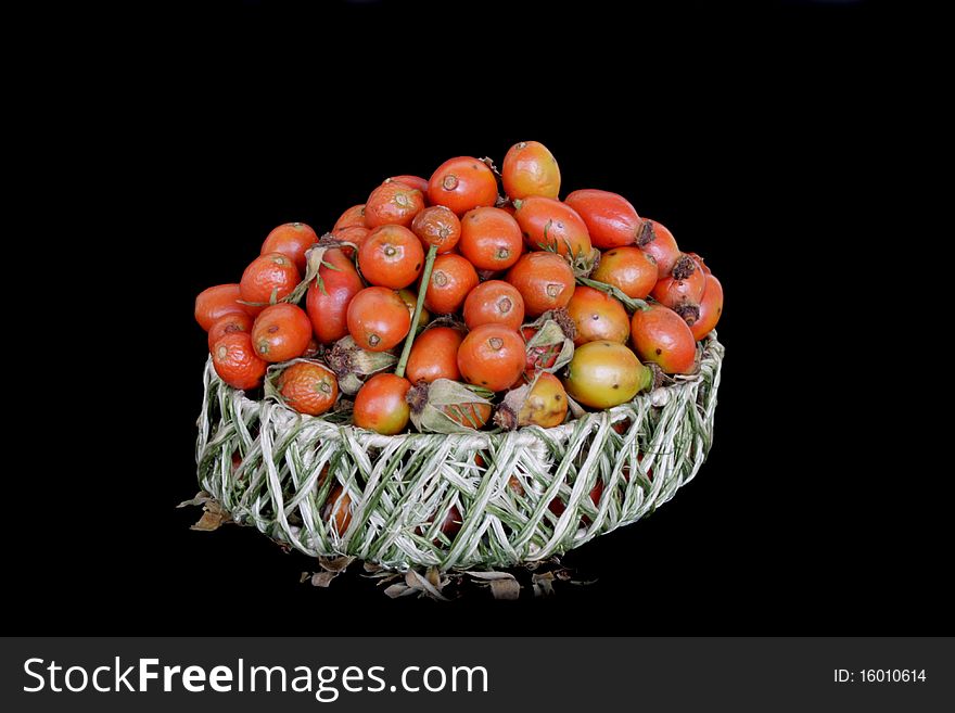 Ripe berries of dog-rose in wicker basket in isolated over black