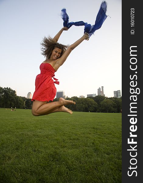 A happy woman wearing red with a blue scarf jumps for joy in a city park. A happy woman wearing red with a blue scarf jumps for joy in a city park