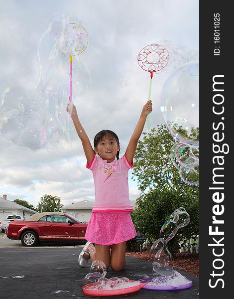 Young girl in a parking lot playing and making bubbles with wands in both hands. Young girl in a parking lot playing and making bubbles with wands in both hands.