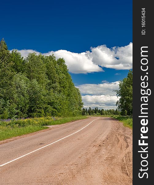 Empty dusty road in rural place under deep blue sky with some clouds