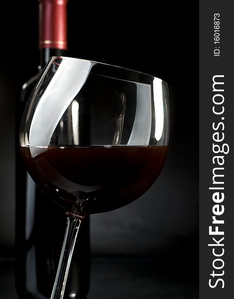 Bottle and glass of red wine on a dark background