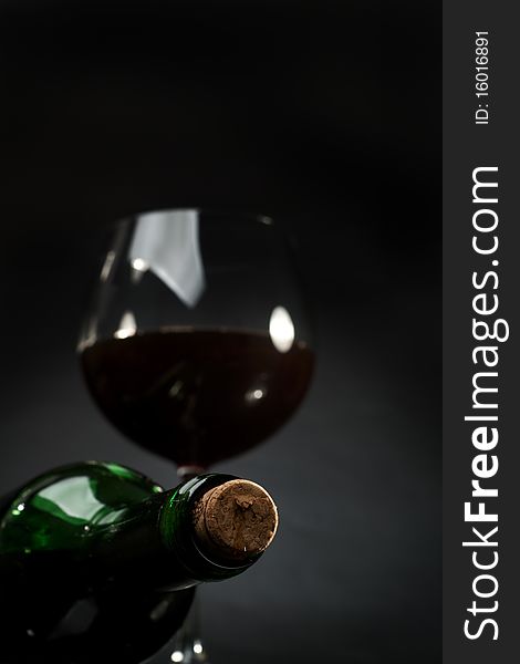Bottle and glass of red wine on a dark background