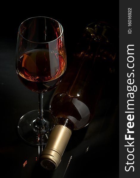 Bottle and glass of white wine on a dark background