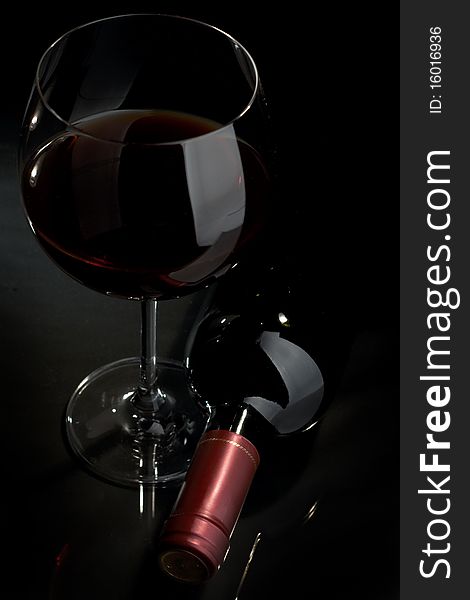 Bottle and glass of red wine on a dark background