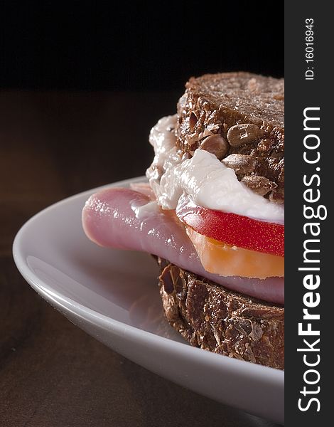 Close-up of a sandwich with turkey, cheese, tomato, and mayo on a white plate.