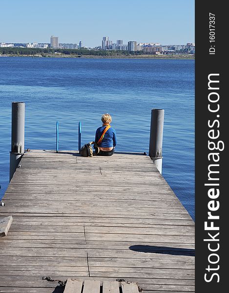 The girl spends his free time, she sits on the pier 
overlooking the water and city in the distance. The girl spends his free time, she sits on the pier 
overlooking the water and city in the distance