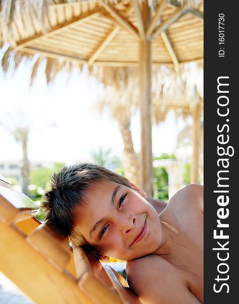 Smiling teenage boy portrait lying under sunshade on beach. Smiling teenage boy portrait lying under sunshade on beach