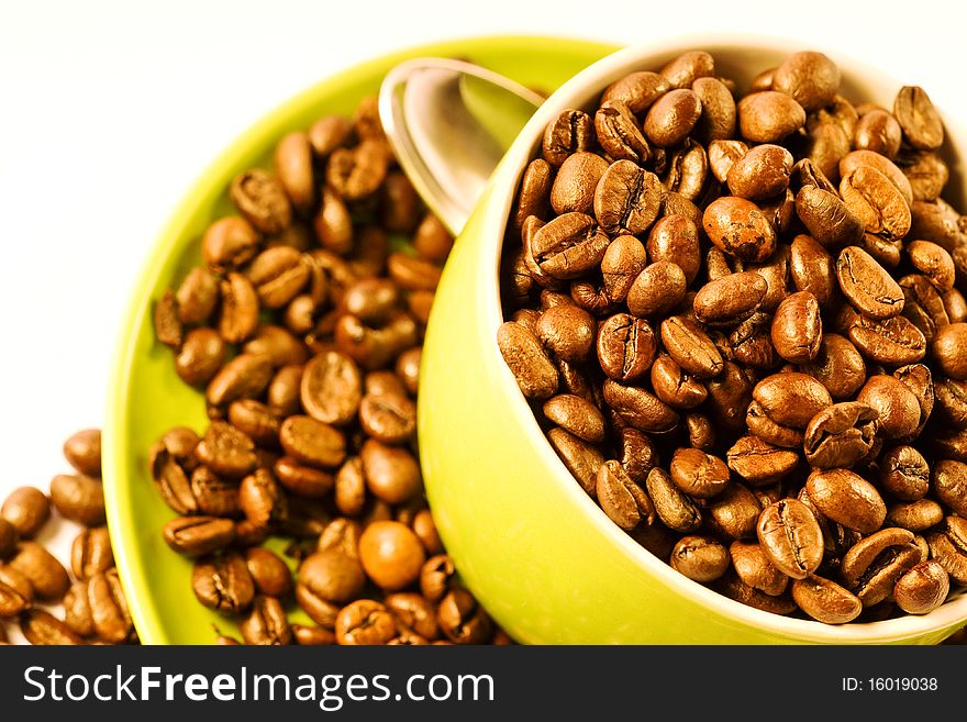 Green cup of coffee with brown beans on white ground