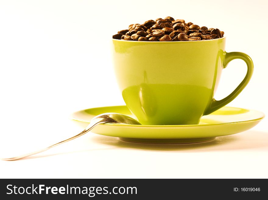 Green cup of coffee with brown beans on white ground