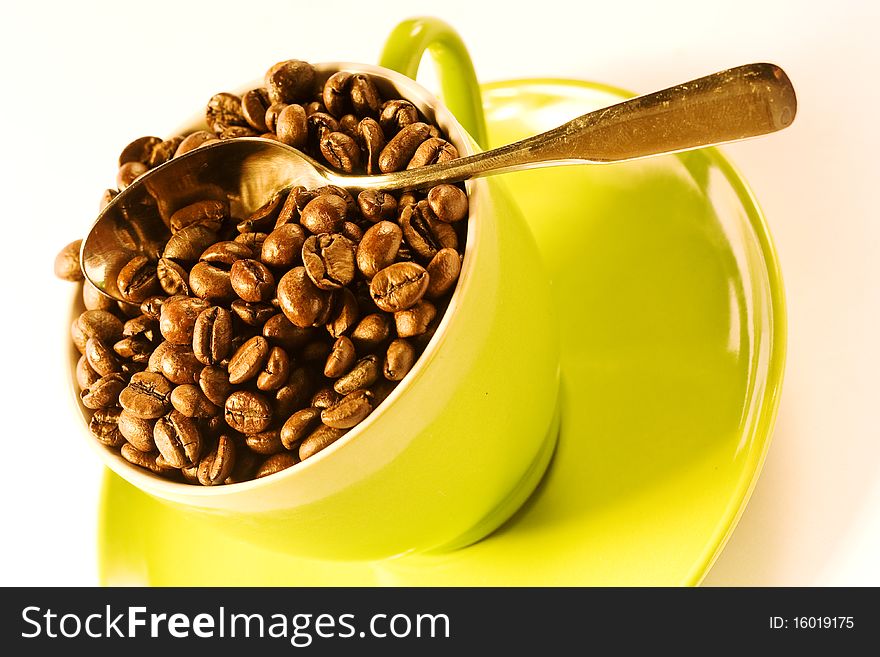 Green cup of coffee with brown beans on white ground