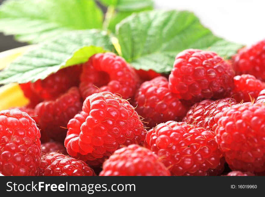 Ripe red raspberries with green leaves close up