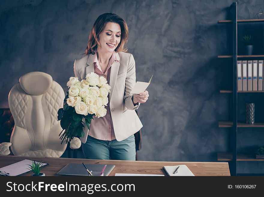 Portrait of her she nice attractive cheerful cheery mature lady holding in hands white roses, reading romance post card professional holiday day at industrial style interior work place station. Portrait of her she nice attractive cheerful cheery mature lady holding in hands white roses, reading romance post card professional holiday day at industrial style interior work place station