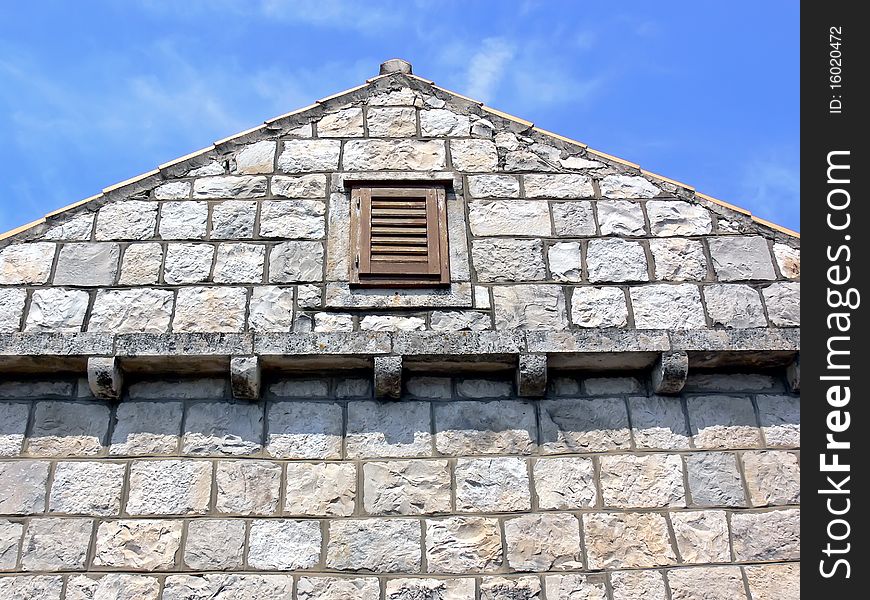 Small window on the top of the stone wall with the blue sky in background.