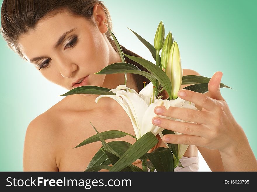 A young and attractive brunette woman with a beautiful lily flower. The image is isolated on a light green gradient background. A young and attractive brunette woman with a beautiful lily flower. The image is isolated on a light green gradient background.