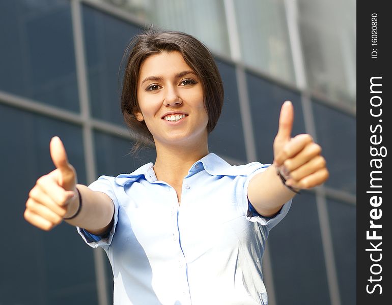 A young and happy businesswoman in formal clothes is holding thumbs up. The image is taken on an abstract background. A young and happy businesswoman in formal clothes is holding thumbs up. The image is taken on an abstract background.